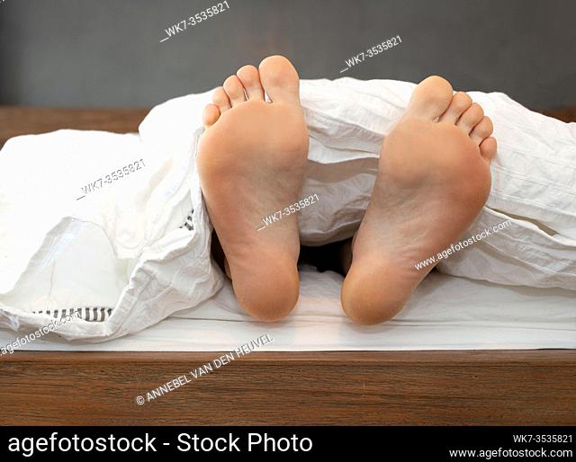 One pair of Feet alone in Bed on White Sheets sleeping under a blanket, relaxion cute