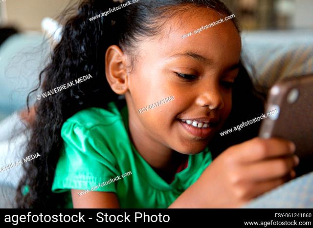 Close-up of african american elementary girl using digital tablet while lying on couch in school