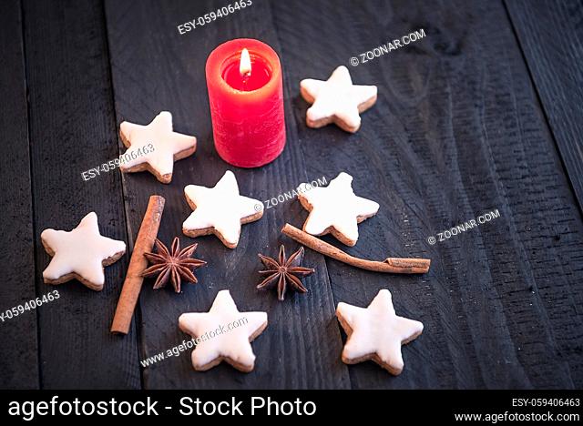 Homemade cinnamon and nuts cookies, star shaped, with decorative spices between them, on an old black wooden table, under the candlelight