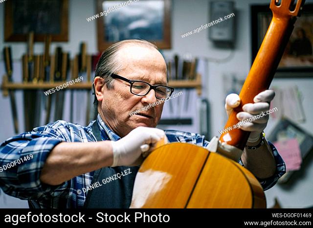 Senior men polishing guitar while standing at workshop