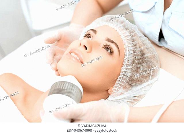 The doctor treats the girl's face with a photoepilator. The girl is lying on the couch in a modern cosmetology salon. She smiles