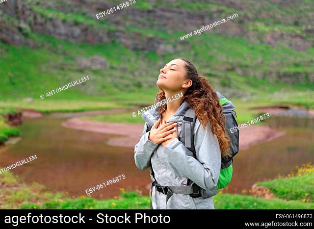 Relaxed hiker breathing fresh air with hands on chest in nature