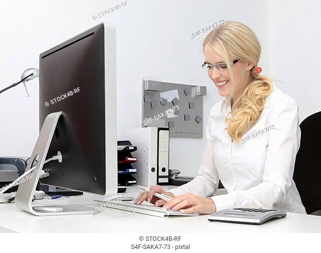 Smiling young woman in office using computer