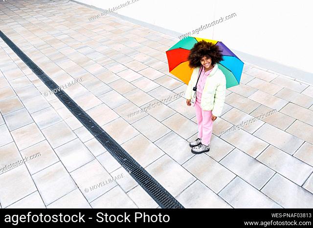 Girl with multi colored umbrella standing on footpath