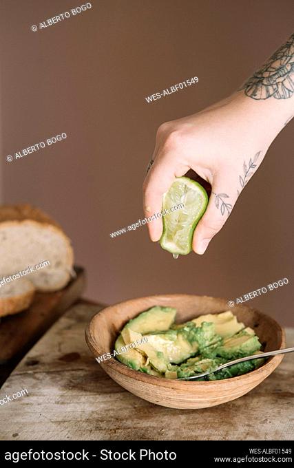 Woman hand squeezing lime in avocado salad kept on cutting board at kitchen