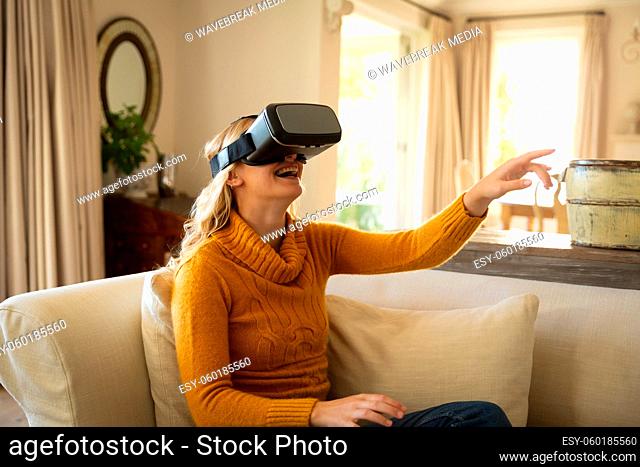 Caucasian woman sitting on couch in luxury living room wearing vr headset, laughing with hand raised