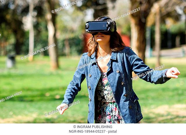 Woman looking in VR glasses and gesturing with his hands outdoors in urban park