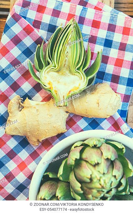 Ripe organic artichokes with lemon and ginger in ceramic bowl on the rustic wooden lattice