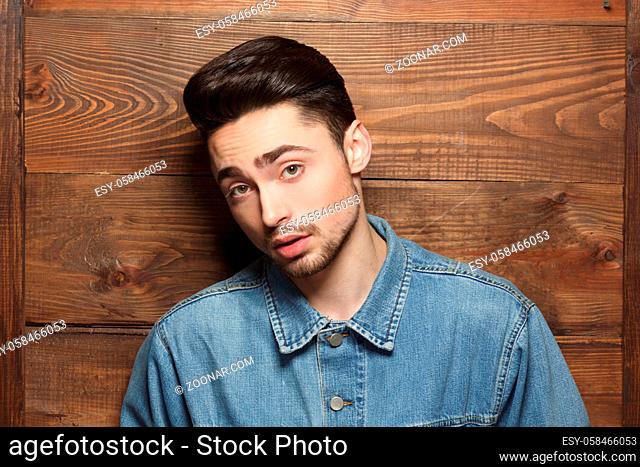 Portrait of handsome model man in jeans shirt posing over wooden background while demonstarting his modern hairstyle in studio