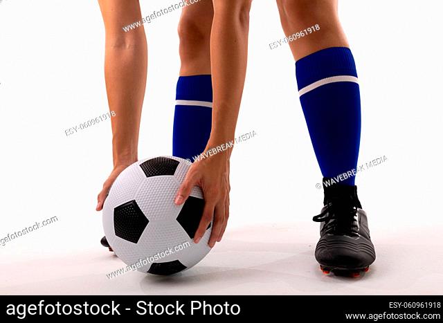 Low section of biracial female player holding soccer ball while standing against white background