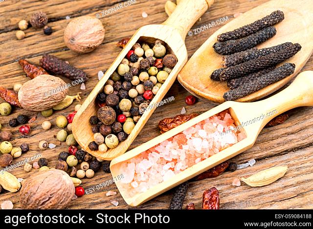 Closeup of spice scoops and a wooden cooking spoon with various exotic spices and further spices in the background on a rustic wood background