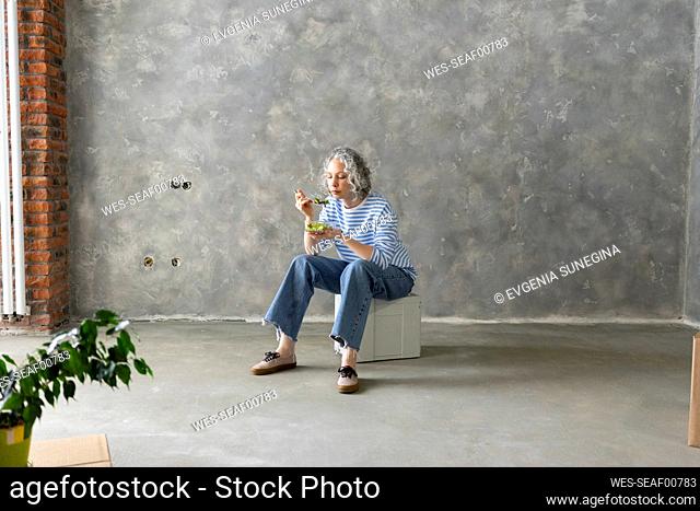 Woman eating lunch sitting on box in front of wall