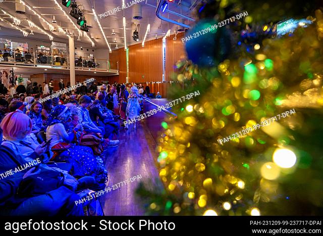 09 December 2023, Bavaria, Coburg: Numerous people in costumes sit next to each other, a Christmas tree is festively decorated