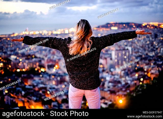 Young woman sitting on railing above the city using cell phone, Barcelona, Spain