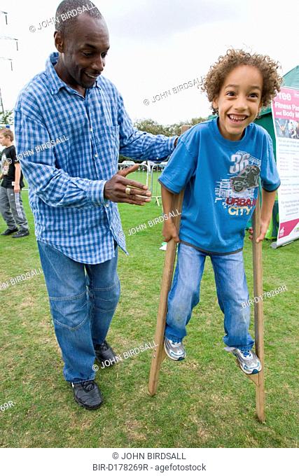 Father helping son to walk on stilts at a Parklife summer activities event