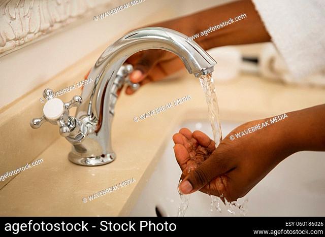 Midsection of african american woman in bathroom wearing bathrobe washing hands in basin