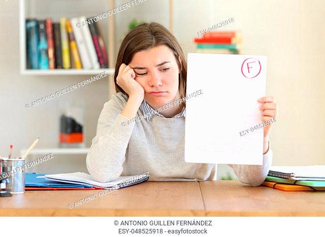 Sad student showing a failed exam to camera at home