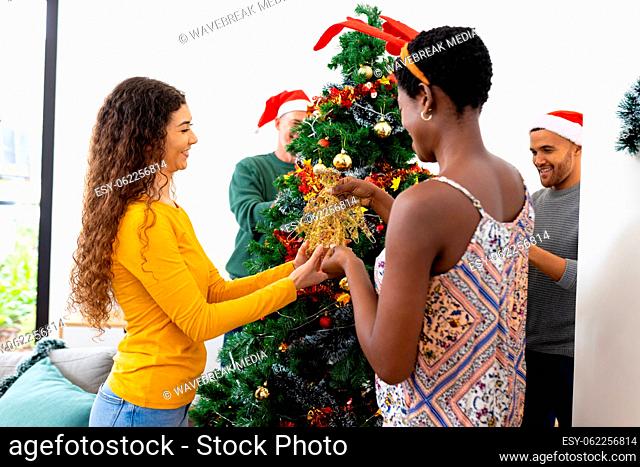 Image of happy diverse friends celebrating christmas at home decorating the tree