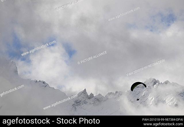 18 October 2020, Bavaria, Garmisch-Partenkirchen: A paraglider flies past the snow-covered peaks of the Wetterstein mountain range