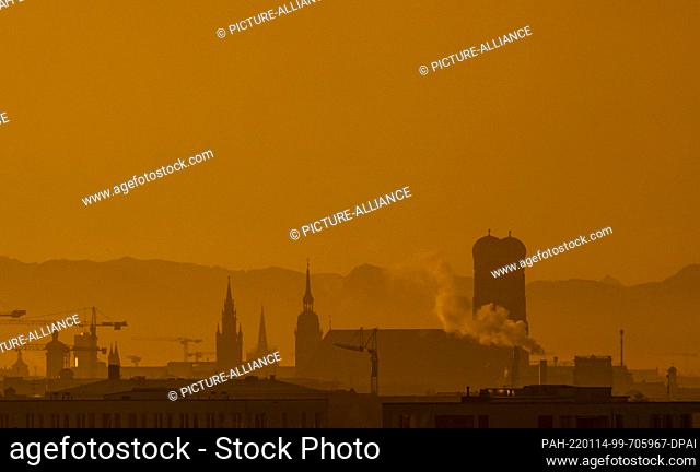 14 January 2022, Bavaria, Munich: The towers of the town hall, the ""Old Peter"" and the Frauenkirche stands in the early morning hours against the backdrop of...