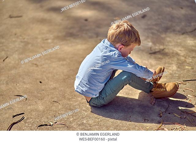 Boy sitting outdoors lacing his boots