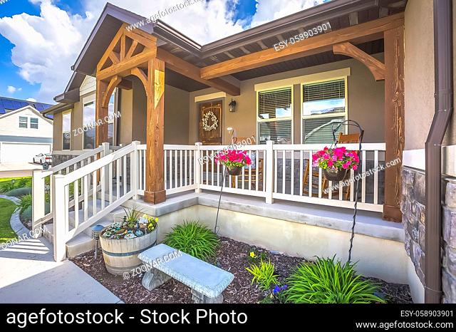 Garden stairs porch and arched entryway at the facade of a home on a sunny day. A white wreath decorates the brown wooden front door