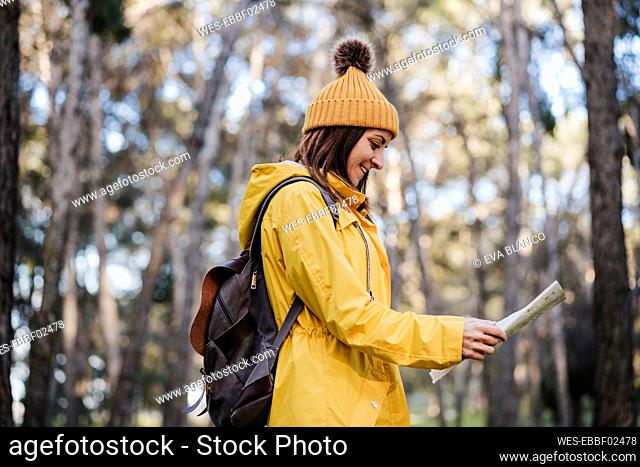 Smiling woman reading map while exploring in forest