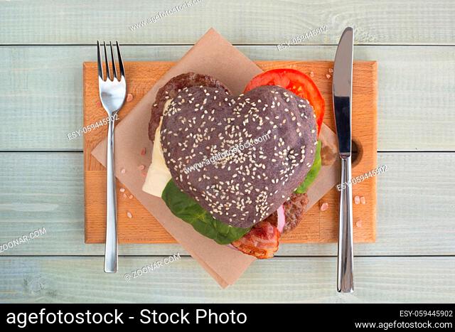 Heart shaped black hamburger, love burger fast food concept, Valentines day surprise dinner, wooden background, top view flat lay