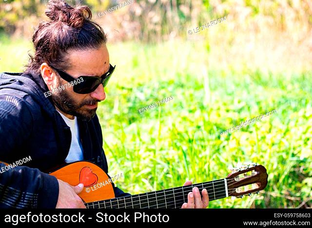 Hippy man with beard and glasses playing guitar outdoors on the grass. High quality photo