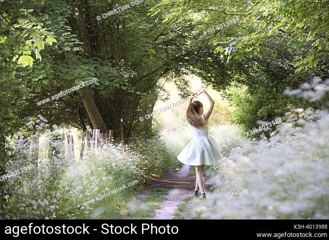 Girl performing a position (5th) of classical dance on a small country trail bordered by umbellifers on the edge of the forest, Eure-et-Loir department
