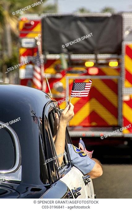 An American flag flutters from the window of an antique 1951 police car as it follows a fire engine in a Fourth of July parade in Newport Beach, CA