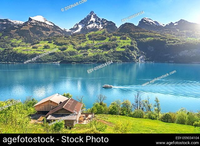 Amazing spring landscape with the Alps mountains, the Walensee lake with a boat floating on it, and an old stable on a green meadow, on a sunny day