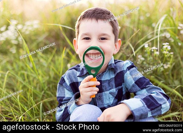 Happy boy with magnifying glass in front of plants