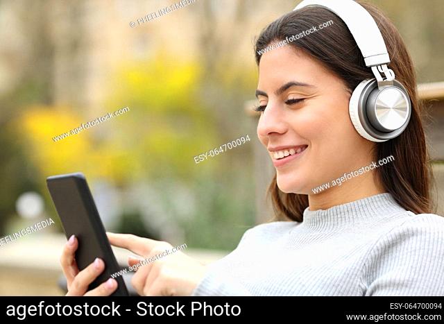 Happy teen listening to music with headphones and smart phone sitting in a park