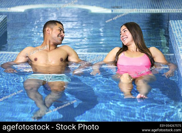 Horizontal indoors shot of young man and woman looking at each other lying and having rest in swimming pool