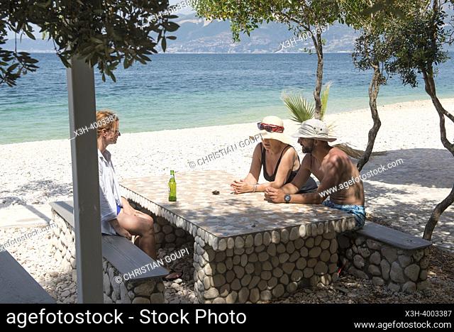 Three persons sitting at a table on the Beach in Zhanpovel Bay, Peninsula of Karaburun, within the Karaburun-Sazan Marine Parc, Vlore bay, Albania