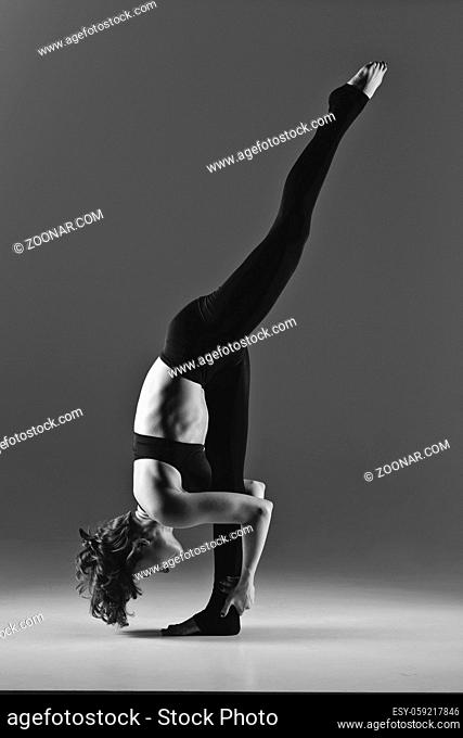 Beautiful young dancer woman warming up. Studio shot on grey background. Copy space. monochrome