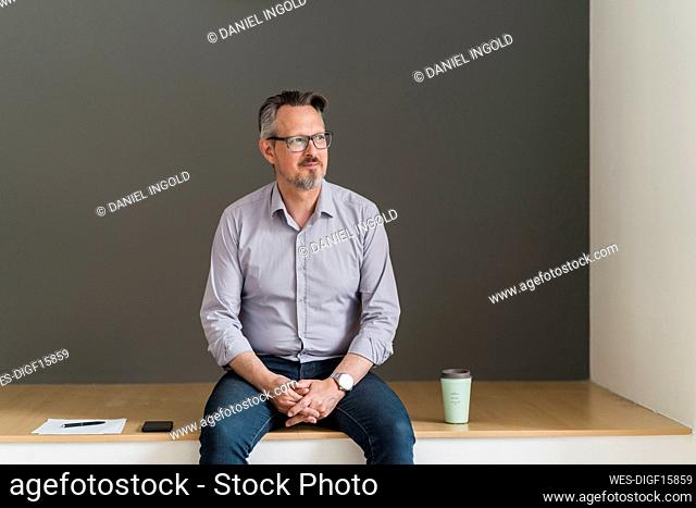 Mature businessman sitting by disposable cup and mobile phone in office