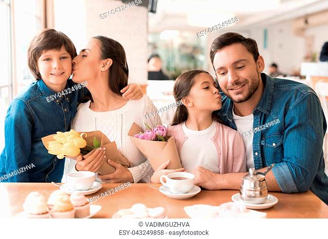 A young family came together in a cafe. They celebrate the holiday. Mom, dad and little daughter drink tea, eat cakes. They are happy together