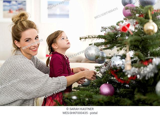 Portrait of smiling woman decorating Christmas tree with her little daughter in the living room