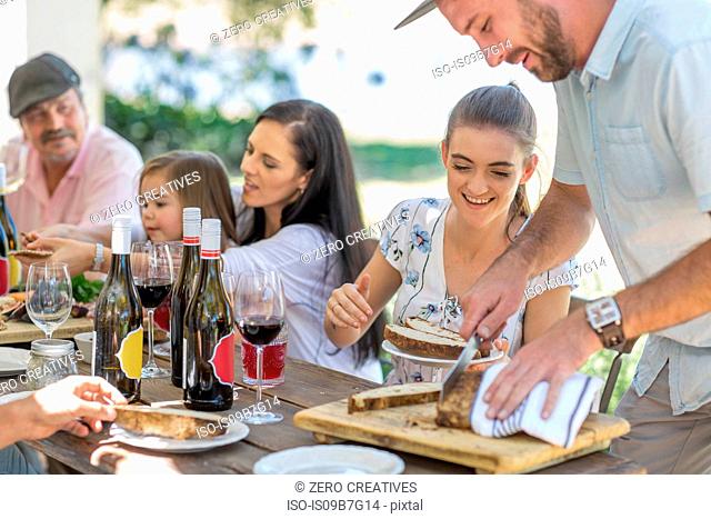 Man slicing bread at outdoor family lunch