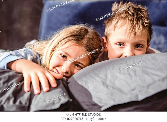 Cute smiling brother and sister lying on grey pillows and looking at camera
