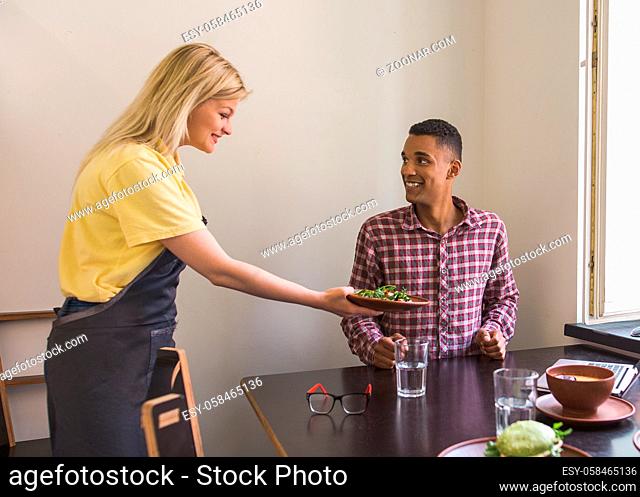 Blond waitress lady giving her guest vegan salad. Vegan concept. Handsome man is being served in vegan restaurant or cafe