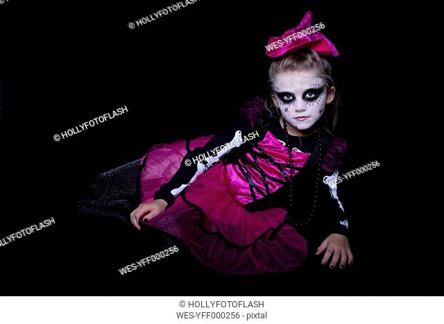 Little girl masquerade as modern undead witch lying in front of black background