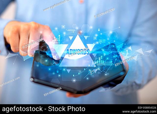 Businessman holding a foldable smartphone with ADWORDS inscription, business concept