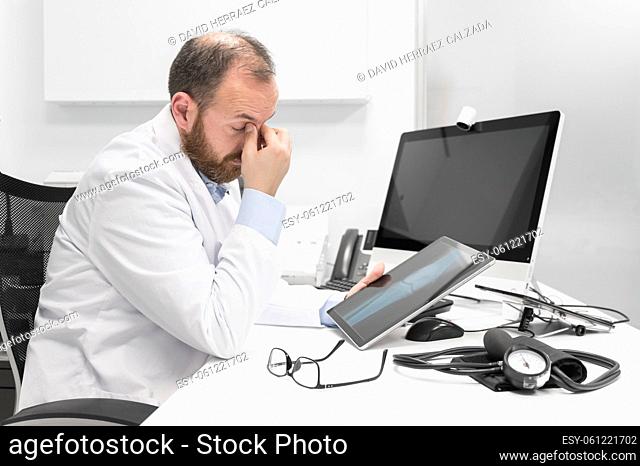 Young doctor rubbing his eyes, feeling tired and unhappy. Health care worker stress and frustration concept. High quality photography