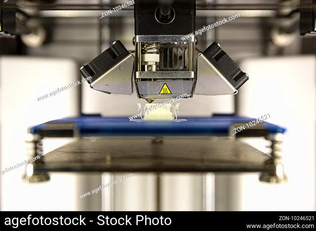 A 3D printer prints a white plastic detail. Three dimensional printing machine