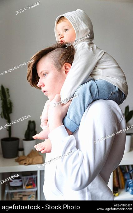 Boy carrying younger sibling on shoulder while looking away at home