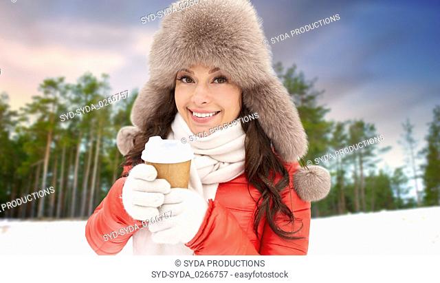 woman in fur hat with coffee over winter forest