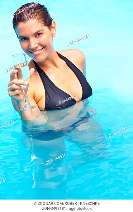 Lachende attraktive Frau mit einem Glas Sekt im Pool